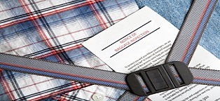 open suitcase with clothing items and notice of baggage inspection on top all secured by buckle 